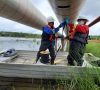 Zwei Männer in einem Boot die unter einer Pipeline stehen, die übers Wasser geht und sie reparieren
